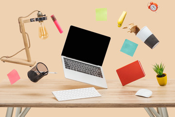 Wall Mural - laptop with blank screen, thermomug with coffee splash and stationery levitating in air above wooden desk isolated on beige