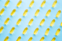 Fish Oil Capsules On Light Pastel Blue Table. Yellow, Transparent Nutritional Supplements Pattern. Medical, Pharmacy And Healthcare Concept. Closeup. 
