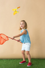 Wall Mural - cute kid catching butterfly with red butterfly net on beige background