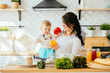 © Iryna - Kid and mother cooking together. Mother holding her little toddler girl and playing in a white kitchen with modern oven. They ares making salad with peppers for dinner.