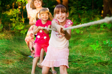 Wall Mural - Group of happy children playing tug of war outside on grass. Kids pulling rope at park.