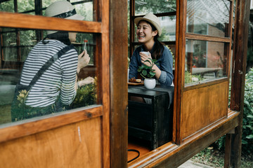 Wall Mural - communication and friendship concept. smiling young asian women with tea bowls in chado shop outdoor cafe. girl best friends laughing chatting talking cheerful relax in japanese old wooden house zen