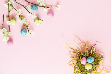 Painted eggs in nest and floral branches lying on pink paper background. Easter decoration. Flat lay. Top view.