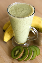 Wall Mural - Fresh kiwi and banana smoothie in glass on the wooden table in the white kitchen with copy space, healthy eating concept