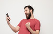 © lashkhidzetim - Portrait of a cheerful young man wearing casual clothes standing isolated over grey background, using mobile phone