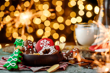 Gingerbread mittens, little man, snowflakes, christmas trees in a brown wooden plate and a bottle of milk on a green wooden on the background of blurred garland. close up. space