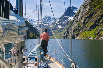 Wall Mural - young woman on lookout at the bow of a sailing yacht, entering the famous Troll Fjord in the Lofoten Islands, northern Norway