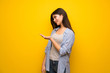 © luismolinero - Teenager girl over yellow wall presenting an idea while looking smiling towards