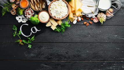 Wall Mural - Products containing natural calcium: cheese, milk, parmesan, sour cream, fish, almonds, parsley, garlic, broccoli. On a black wooden background. Top view. Free copy space.