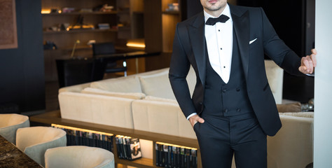 Man model in expensive custom tailored tuxedo, suit standing and posing indoors