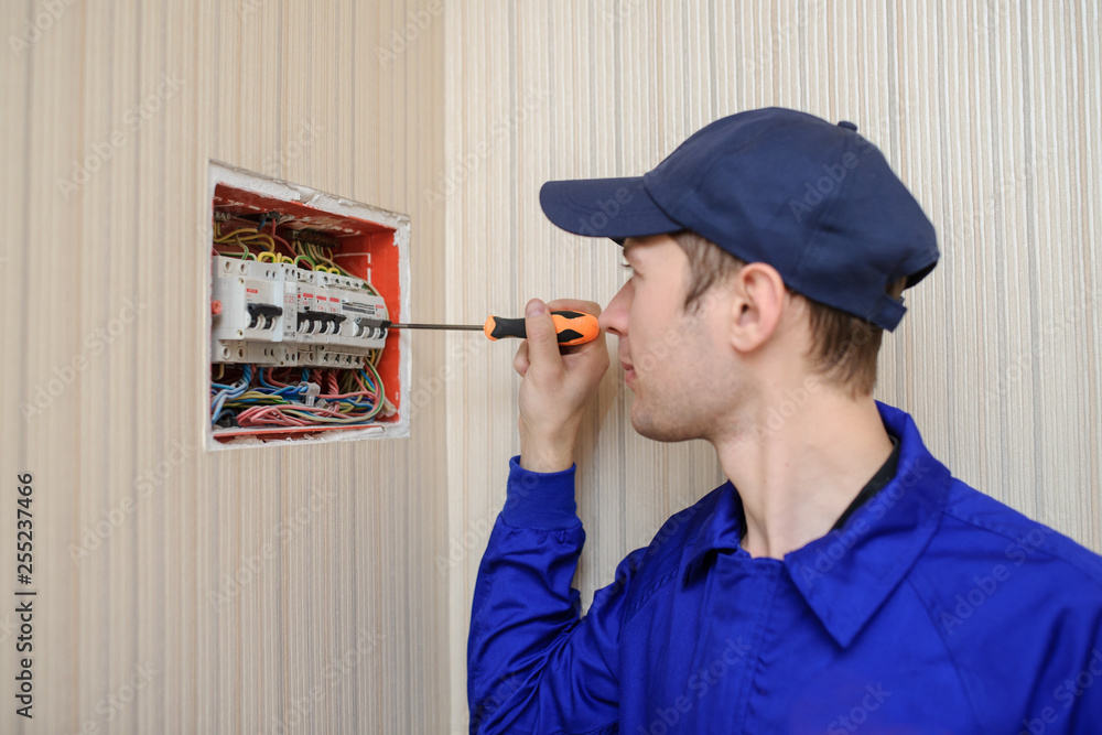 lateral view of a young eletrician in blue overall disassembling a ...