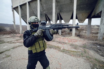 Armed special forces soldier in dark uniform and helmet aiming a rifle in front of ruined building