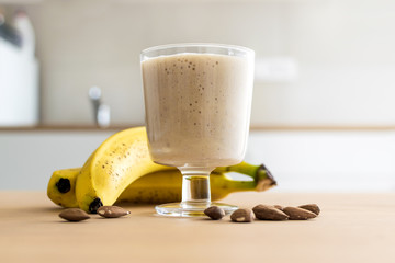 Wall Mural - Fresh banana smoothie in glass on the wooden table in the white kitchen with copy space, healthy eating concept