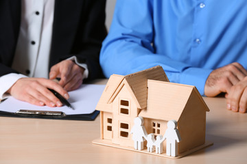 Real estate agent working with client at table, focus on house and family figures. Home insurance