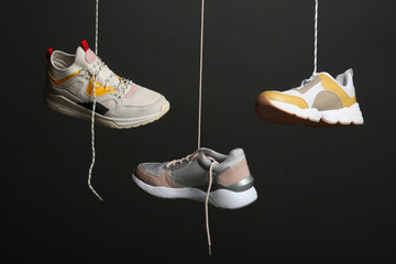 Different sneakers hanging on black background. Stylish shoes