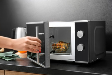 Young woman using microwave oven on table in kitchen