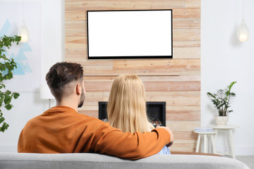 Wall Mural - Couple watching TV on sofa in living room with decorative fireplace