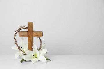 wooden cross, crown of thorns and blossom lilies on table against light background, space for text