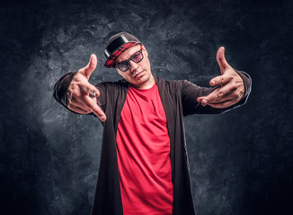 Portrait of a young rapper dressed in a hip-hop style, posing for a camera. Studio photo against a dark textured wall