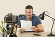 © triocean - Young smiling cheerful man sitting at the office desk in front of the camera making a video. Male blogger recording a video tutorial.
