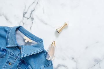 Denim jacket and bottle of perfume on marble background. Flat lay design composition with feminine clothing and accessories. Beauty blogger, trendy hipster lifestyle.