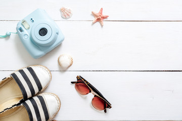 Summer holiday composition, traveler accessories on white wooden desk: sunglasses, sandals, instant camera, sea shell and star. Vacation, relaxing, sea beach resort, summer holidays concept