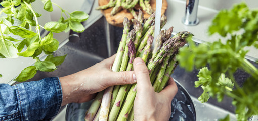 cropped shot of male hands in soil washing fresh asparagus in kitchen sink