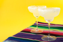 Happy Cinco De Mayo, Mexico Fiesta And Cocktail Party Concept Theme With Two Margaritas And A Mexican Stripped Pattern Rug Named Serape Isolated On Yellow Background With Copy Space
