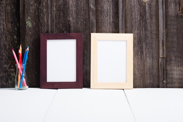 brown painted and natural wood picture frame, pencils, white table, old wooden wall