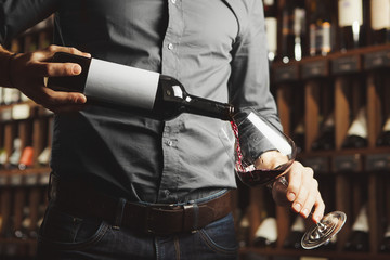 Wall Mural - Close up photo of male sommelier pouring red wine into wineglasses. Waiter with bottle of alcohol beverage.