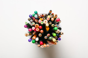 A lot of multi-colored pencils in a glass on a white background. View from above. School or art workshop.