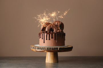 Sweet chocolate cake with sparklers on table against color background