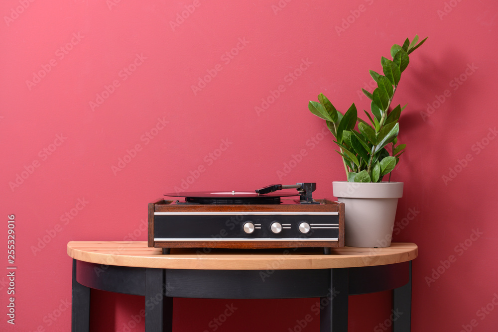 Record player with vinyl disc on table near color wall