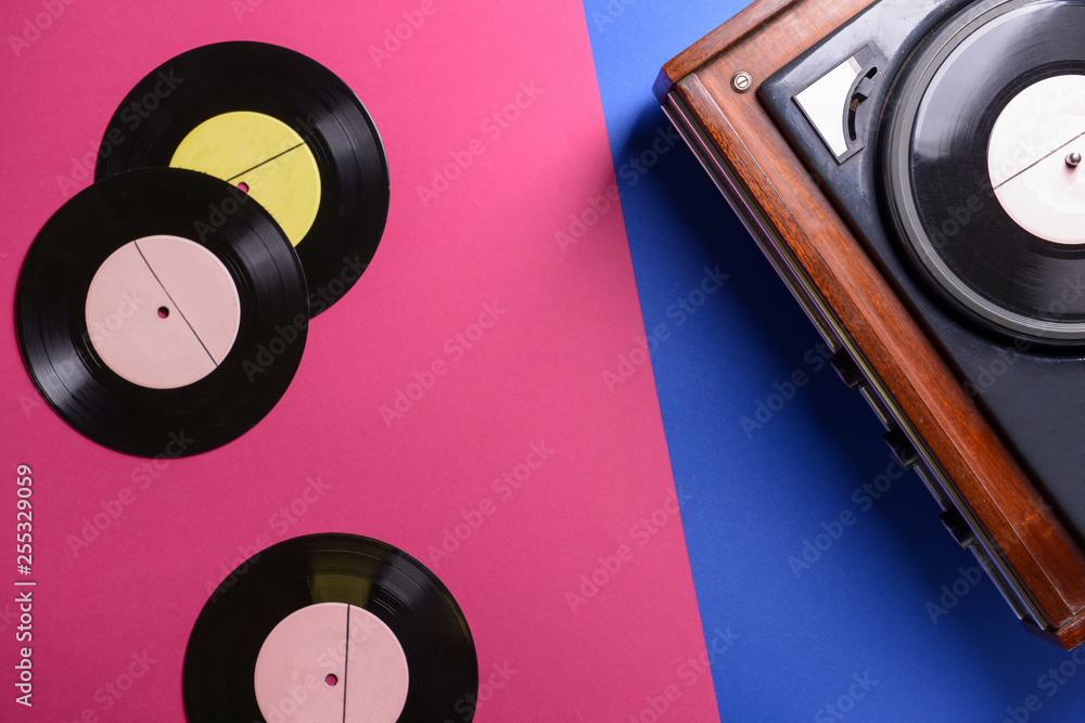 Record player with vinyl discs on color background