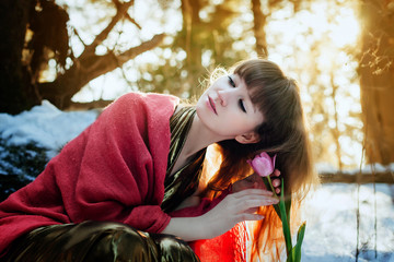 Wall Mural - A beautiful girl in a gold dress sits in a spring Sunny forest and touches a Tulip