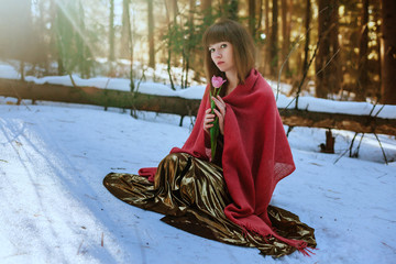 Wall Mural - Beautiful girl in Golden dress sitting in the snow in the spring sun woods and touches Tulip