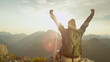 © helivideo - LENS FLARE: Trekker celebrates reaching mountaintop on a sunny summer day.