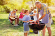 © luckybusiness - smiling grandfather giving grandson grilling meat.
