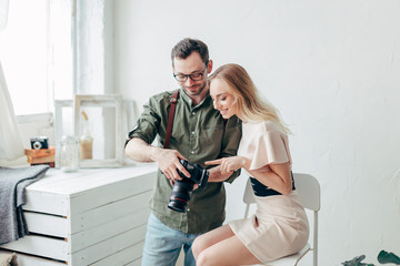 smiling awesome girl poiting at the display of the camera while talking with a professional photographer indoors