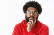 © Cookie Studio - Close-up shot of thoughtful african american man rubbing beard and looking at upper left corner focused, thinking, taking important decision, making choice standing against gray background in glasses