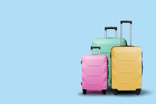 Three Multi-colored Plastic Suitcases On Wheels On A Blue Background. Travel Concept, Vacation Trip, Visit To Relatives
