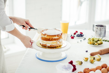 girl smoothing surface using spatula, close up cropped photo. free time. woman spreading the icing to cover the top of the cake