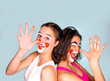 © kravik93 - Two teenage brunettes in t-shirts and with painted faces jokingly show their long noses with their fingers palm. Isolated on gray. Family celebrates April Fool's Day.