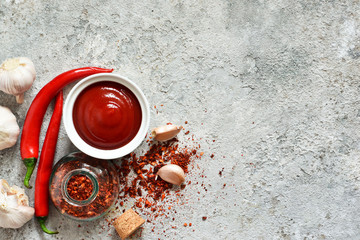 Spicy chili sauce with spices on a concrete background. View from above.