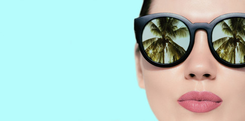 Portrait close up of a pretty woman with reflection of palms in sunglasses  on a bright background