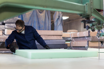 Wall Mural - Young man in a furniture factory is cutting the foam for the sofa