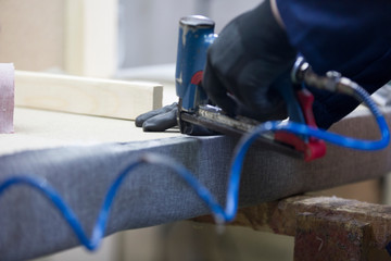 Wall Mural - Closeup of a young man in a furniture factory who puts together one part of the sofa with a stapler