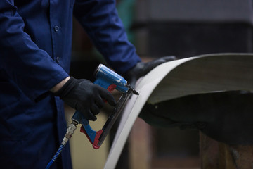 Wall Mural - Closeup of a young man in a furniture factory who puts together one part of the sofa with a stapler