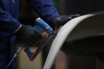 Wall Mural - Closeup of a young man in a furniture factory who puts together one part of the sofa with a stapler