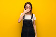 © luismolinero - Woman over yellow wall covering mouth with hands for saying something inappropriate